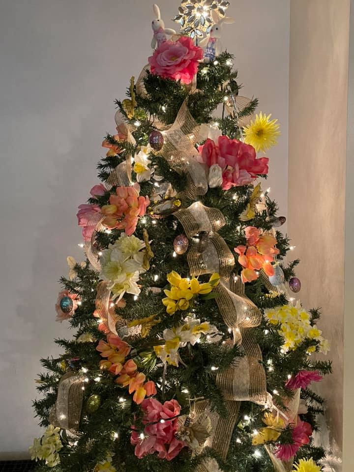 a christmas tree decorated for spring with pink and yellow flowers, butterflies, and burlap