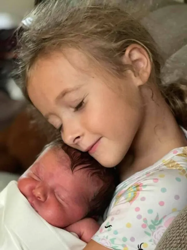 A little girl snuggling a newborn