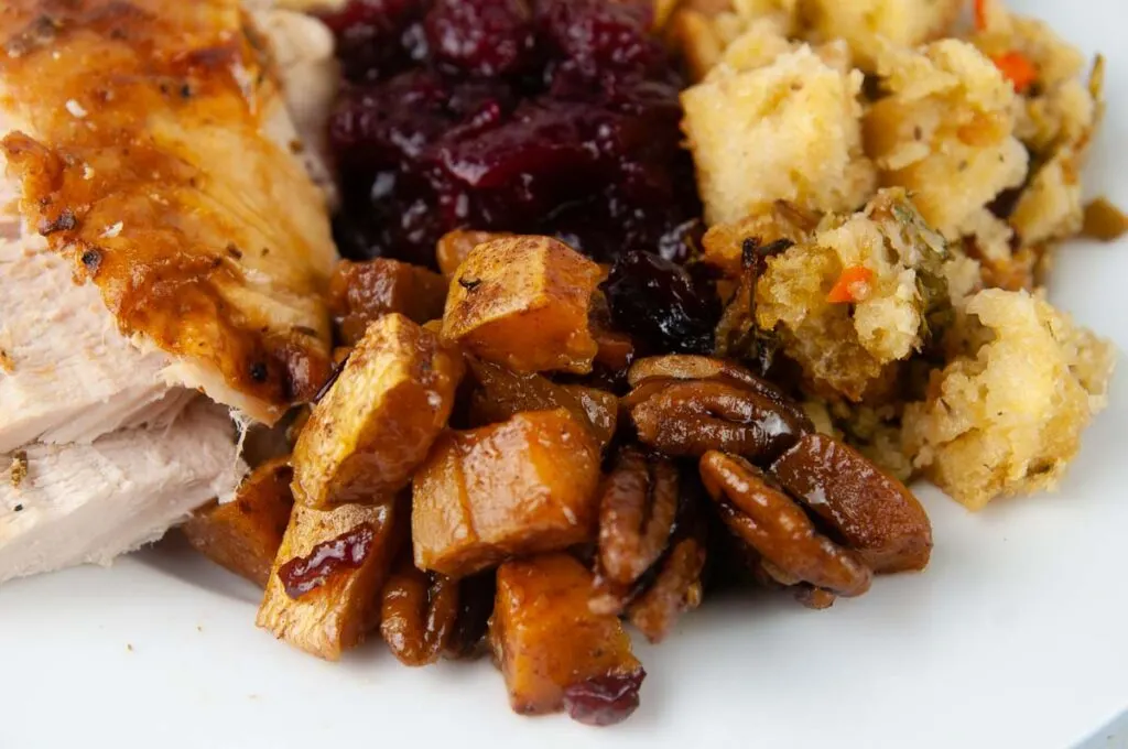 A plate of a turkey dinner featuring turkey breast, cranberry sauce, stuffing and roasted butternut squash.
