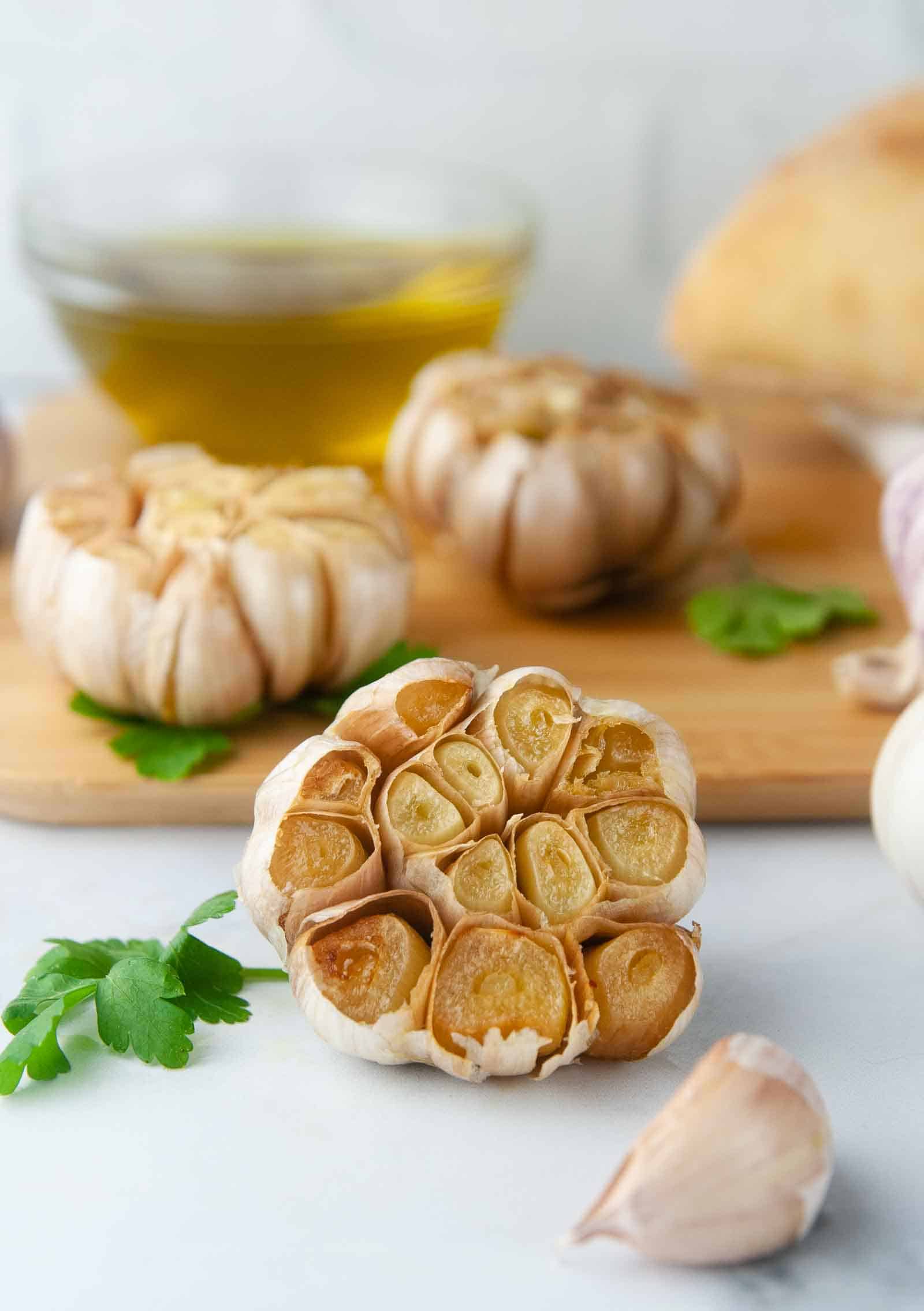 3 heads of roasted garlic  on a wood cutting board in white kitchen