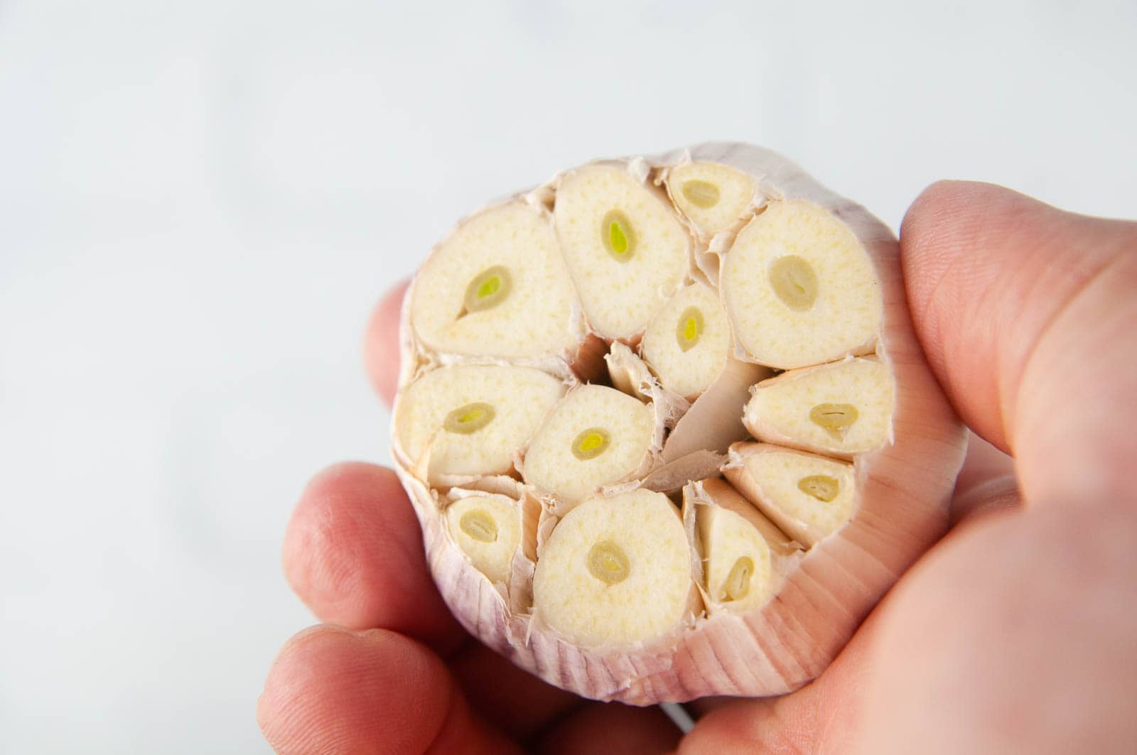 A hand holding garlic with the top cut off