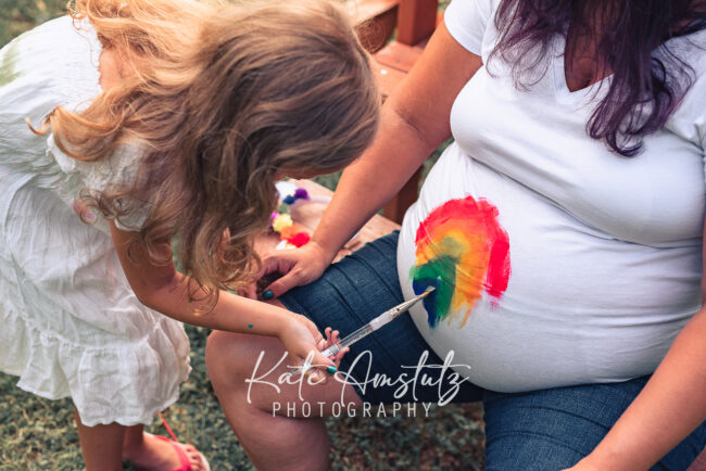 A little girl painting a rainbow on a pregnant woman's belly