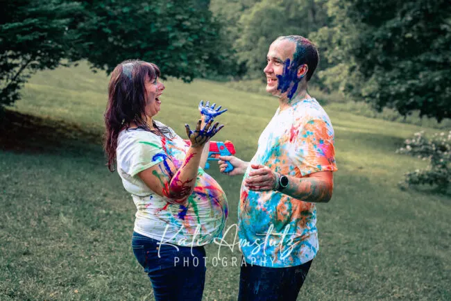 a pregnant woman and her husband covered in rainbow paint