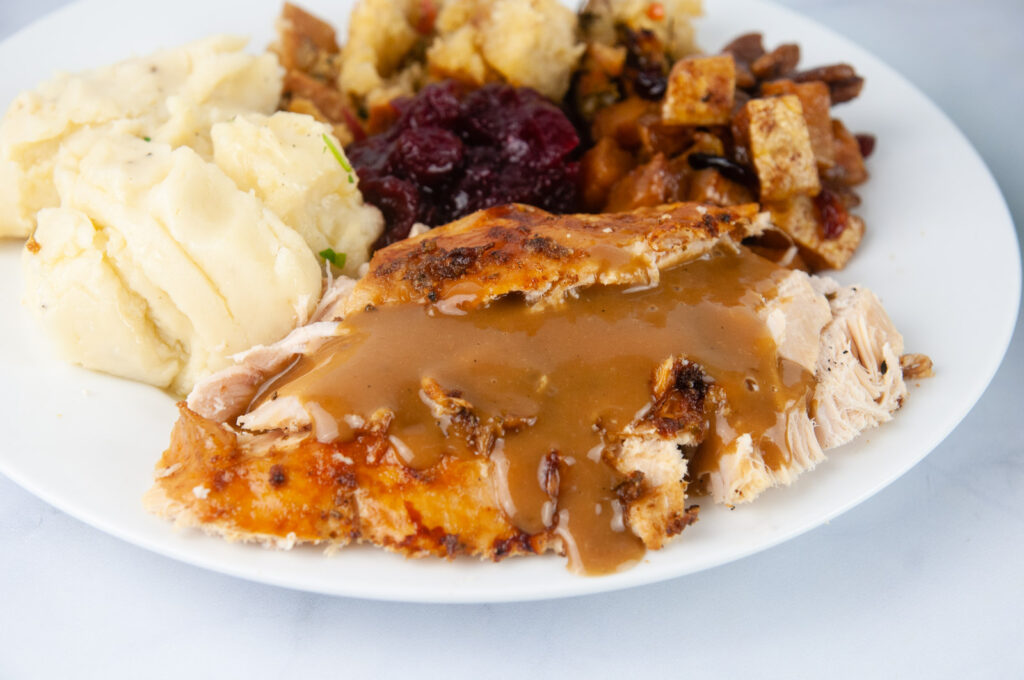 A turkey dinner complete with mashed potatoes, cranberries, stuffing and squash on a white plate