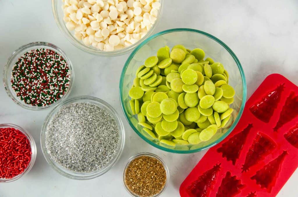 Ingredients for Christmas Tree Candy: Chocolate Chips or Green Candy Melts, Sprinkles, and Coconut Oil next to a silicone mold