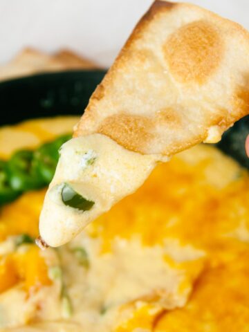A tortilla chip gets dunked into creamy, cheesy jalapeno popper dip.