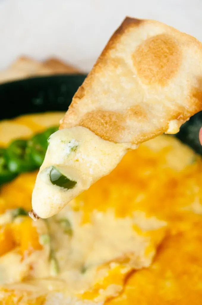 A tortilla chip gets dunked into creamy, cheesy jalapeno popper dip.