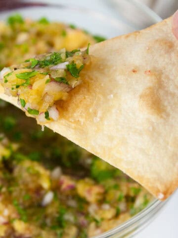Pineapple habanero salsa makes a yummy dip for chips. A tortilla chip being dunked into bowl of pineapple salsa
