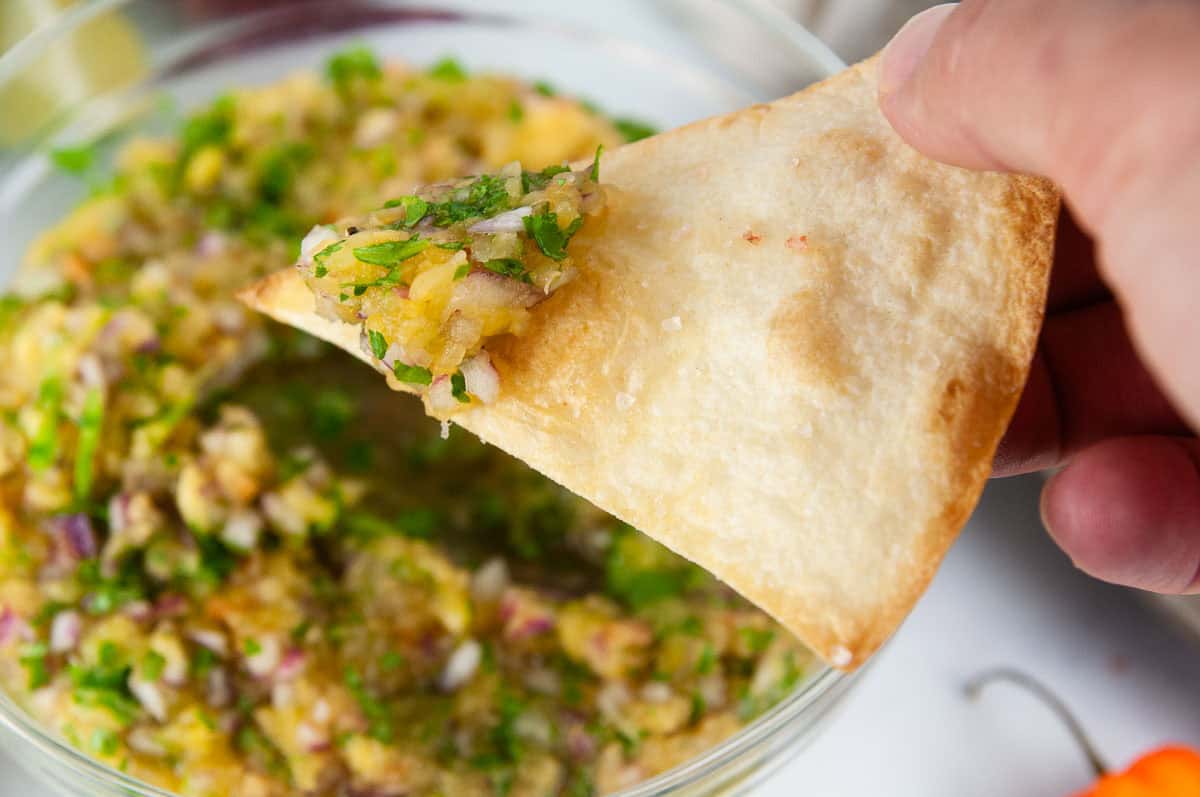 Pineapple habanero salsa makes a yummy dip for chips. A tortilla chip being dunked into bowl of pineapple salsa