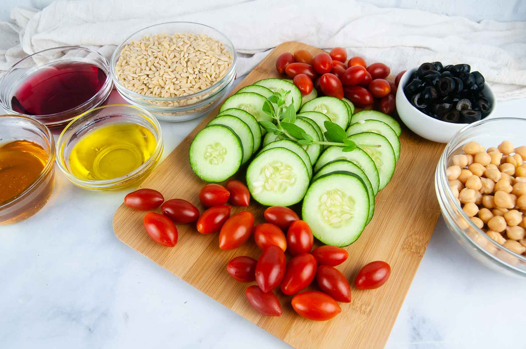 Ingredients for Greek Orzo Salad: orzo, chickpeas, olives, cucumbers, tomatoes, herbs, olive oil, red wine vinegar, honey, and lemon juice