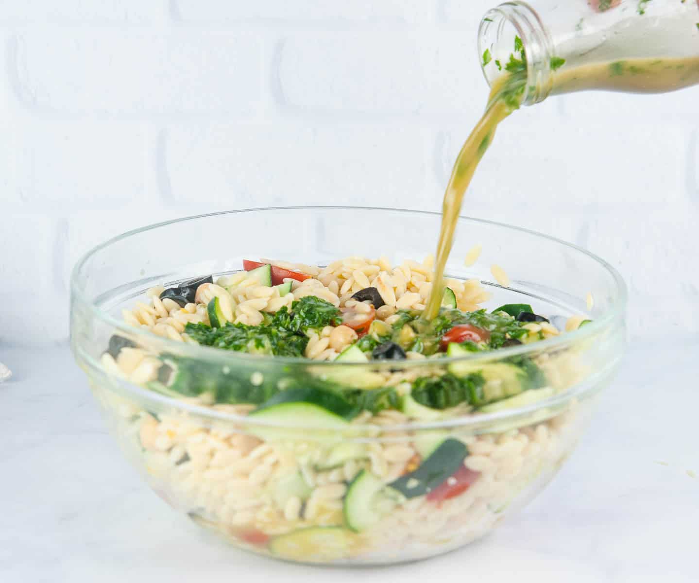 Lemon Red Wine Dressing being poured on Greek orzo salad