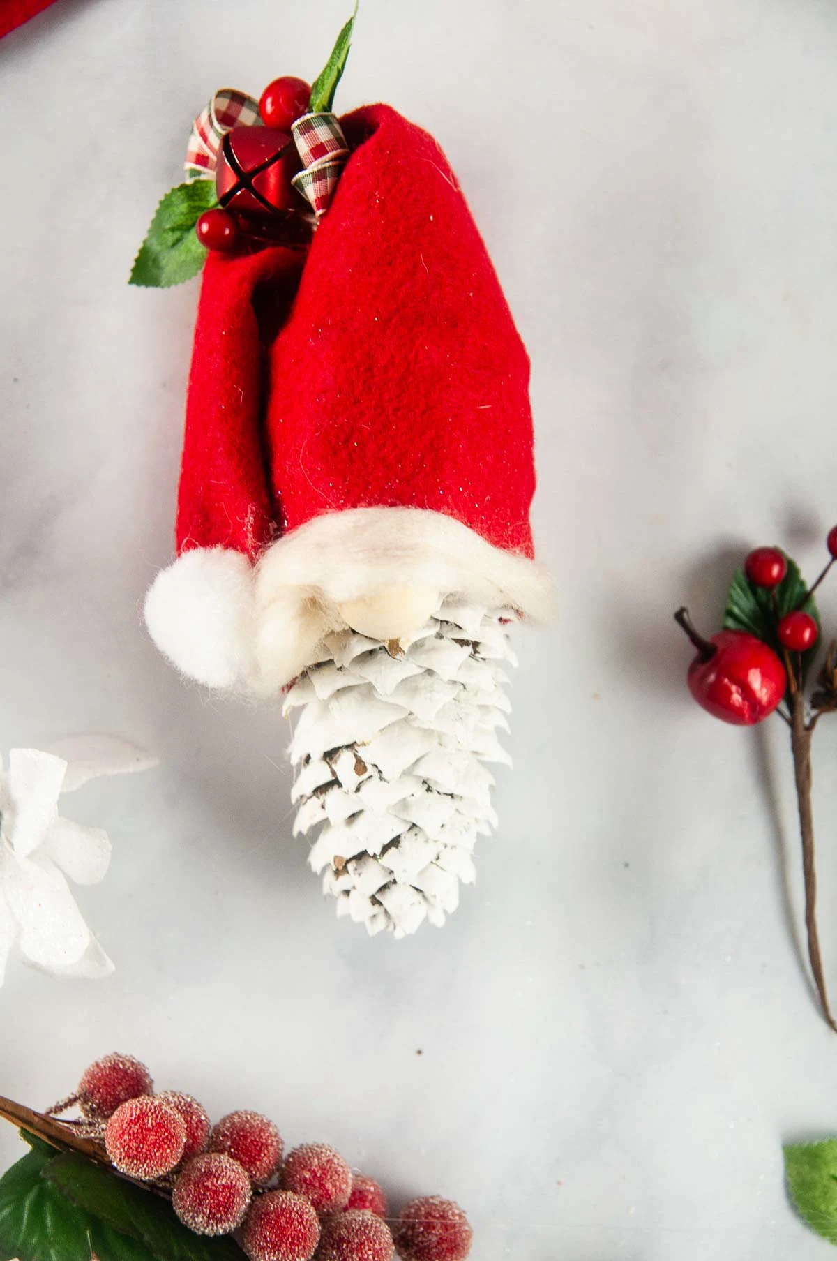 Easy pinecone gnomes are a quick adorable diy gnome ornament. A painted pinecone wears a red felt hat with a puff ball and bow so it looks like a Christmas gnome.