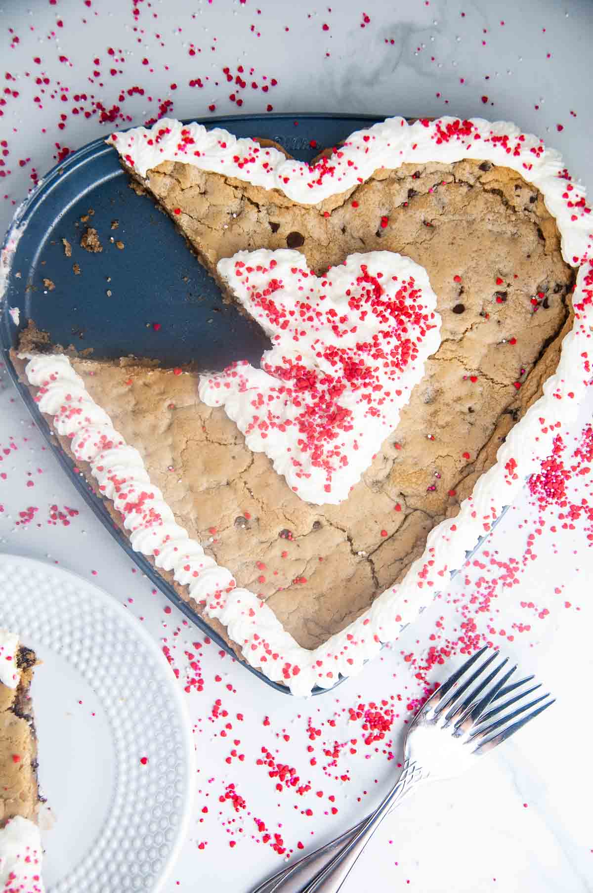 A piece cut out of a heart shaped chocolate chip cookie cake