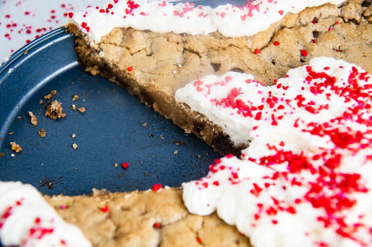 A piece cut out of a heart shaped chocolate chip cookie cake