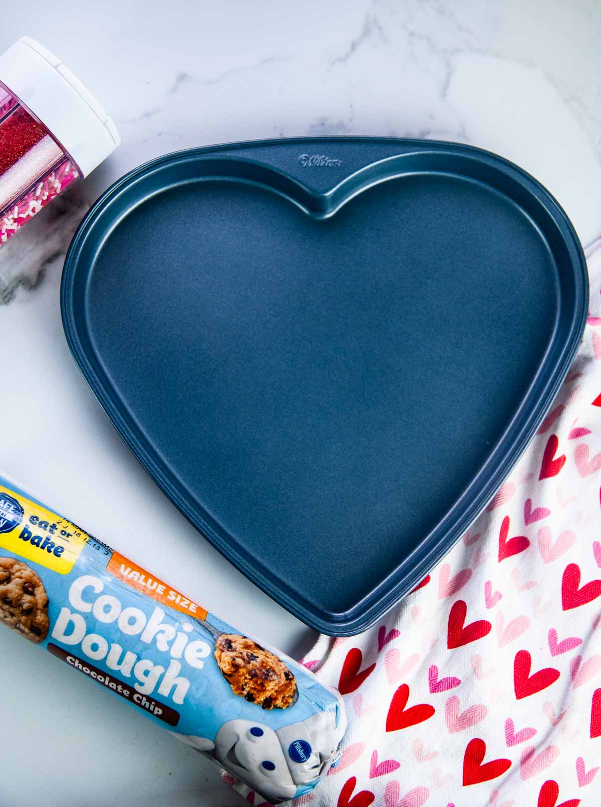 Supplies for a giant heart shaped cookie for Valentine's Day: Cookie Dough, Heart shaped pan, and Sprinkles