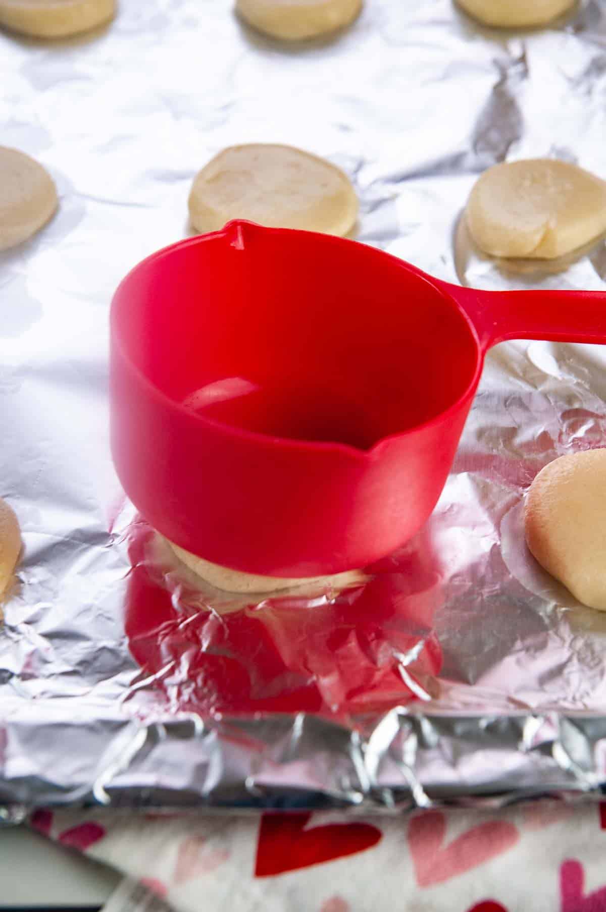 Flatten the sugar cookie dough gently with a measuring cup.