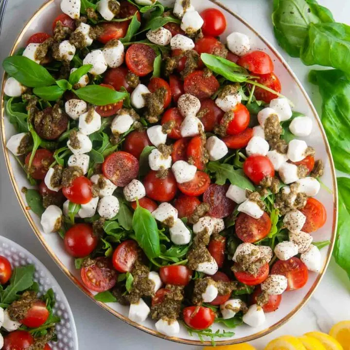 Easy pesto Caprese salad features creamy fresh mozzarella, sweet cherry tomatoes, and aromatic basil all served over sharp arugula and drizzled with lemon pesto.
