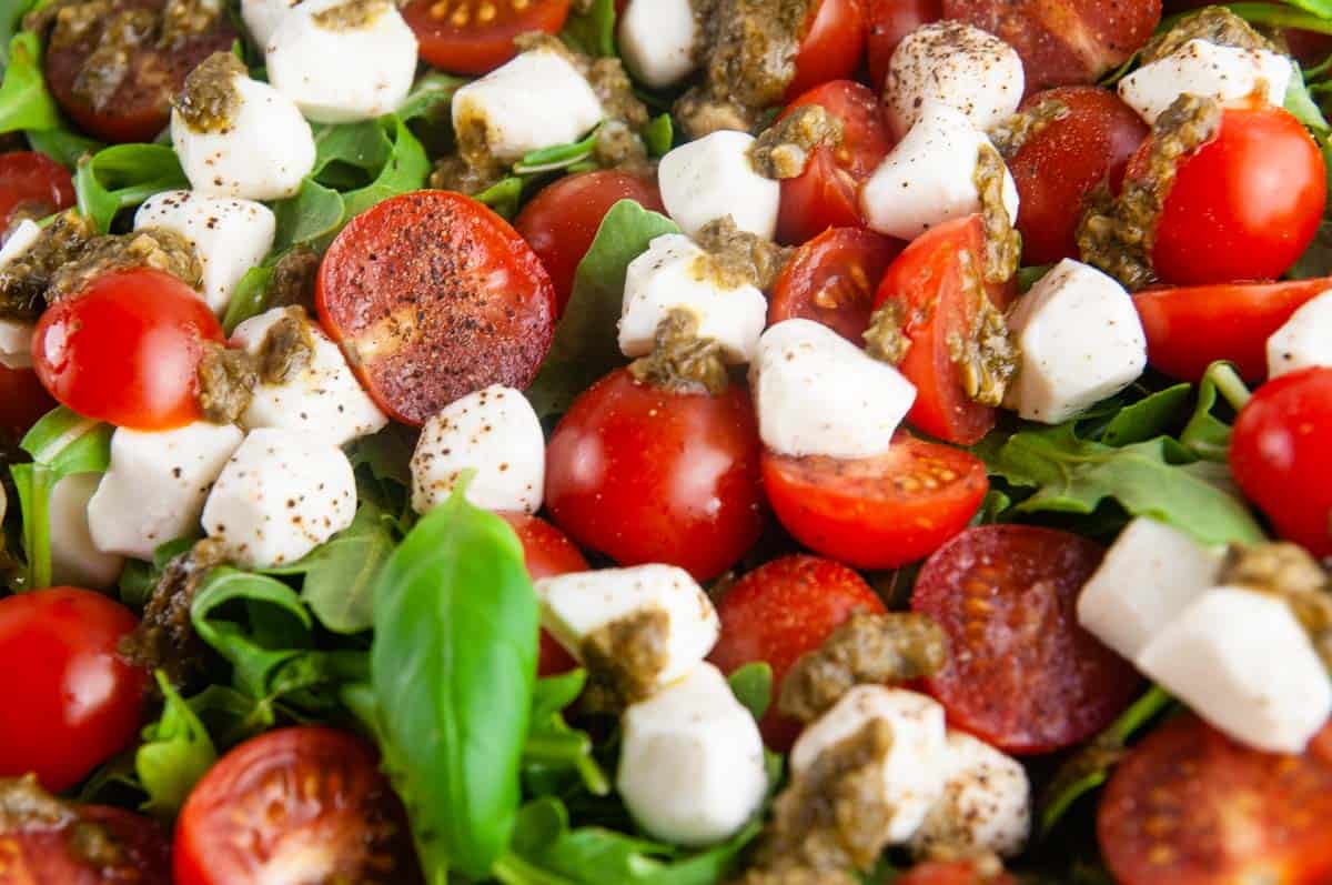 Easy pesto Caprese salad features creamy fresh mozzarella, sweet cherry tomatoes, and aromatic basil all served over sharp arugula and drizzled with lemon pesto.