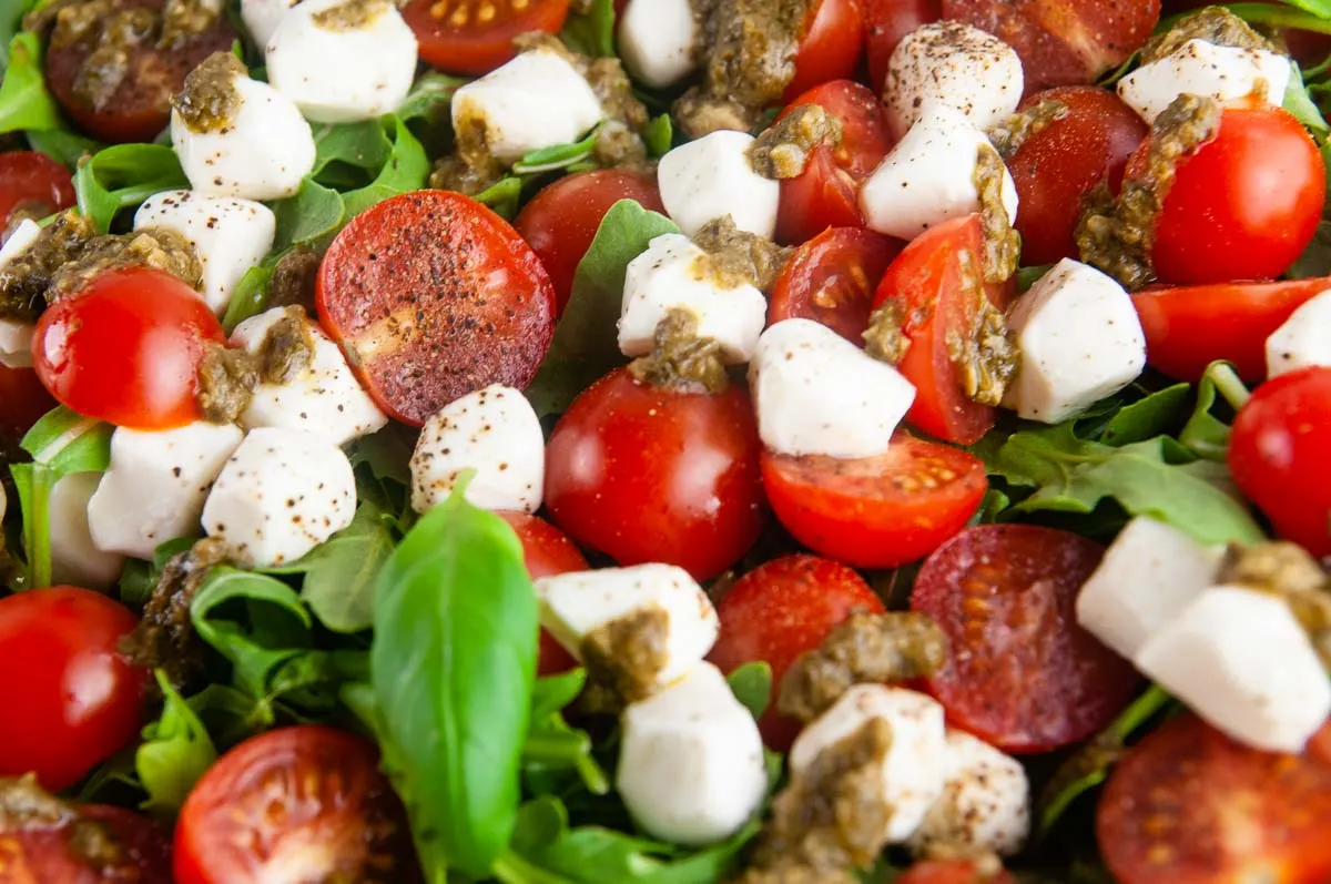 Easy pesto Caprese salad features creamy fresh mozzarella, sweet cherry tomatoes, and aromatic basil all served over sharp arugula and drizzled with lemon pesto.