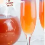 2 cranberry orange mimosas with a pitcher of mimosas behind them set in a red background with text reading Christmas Morning Mimosas