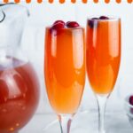 2 cranberry orange mimosas with a pitcher of mimosas behind them set in a red background with text reading Christmas Morning Mimosas