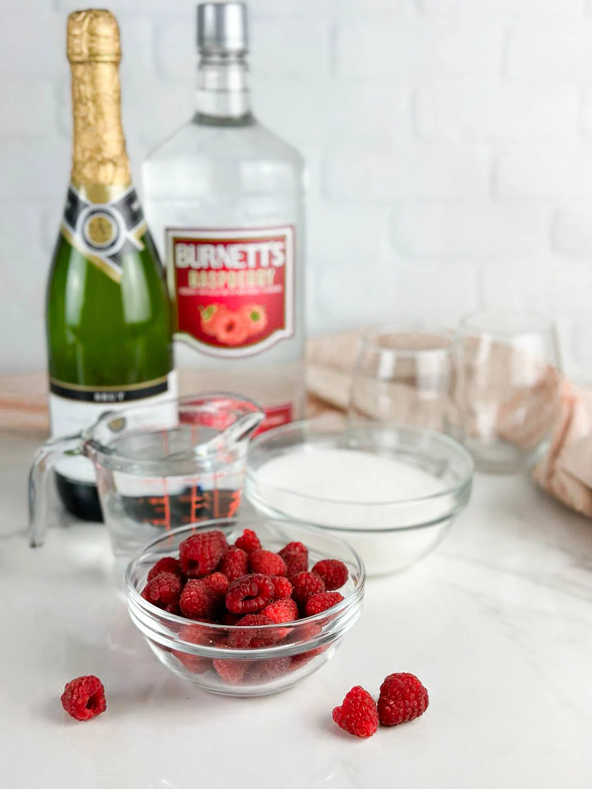 Ingredients for raspberry champagne cocktails: raspberries, sugar, water, raspberry liqueur, and sparkling white wine