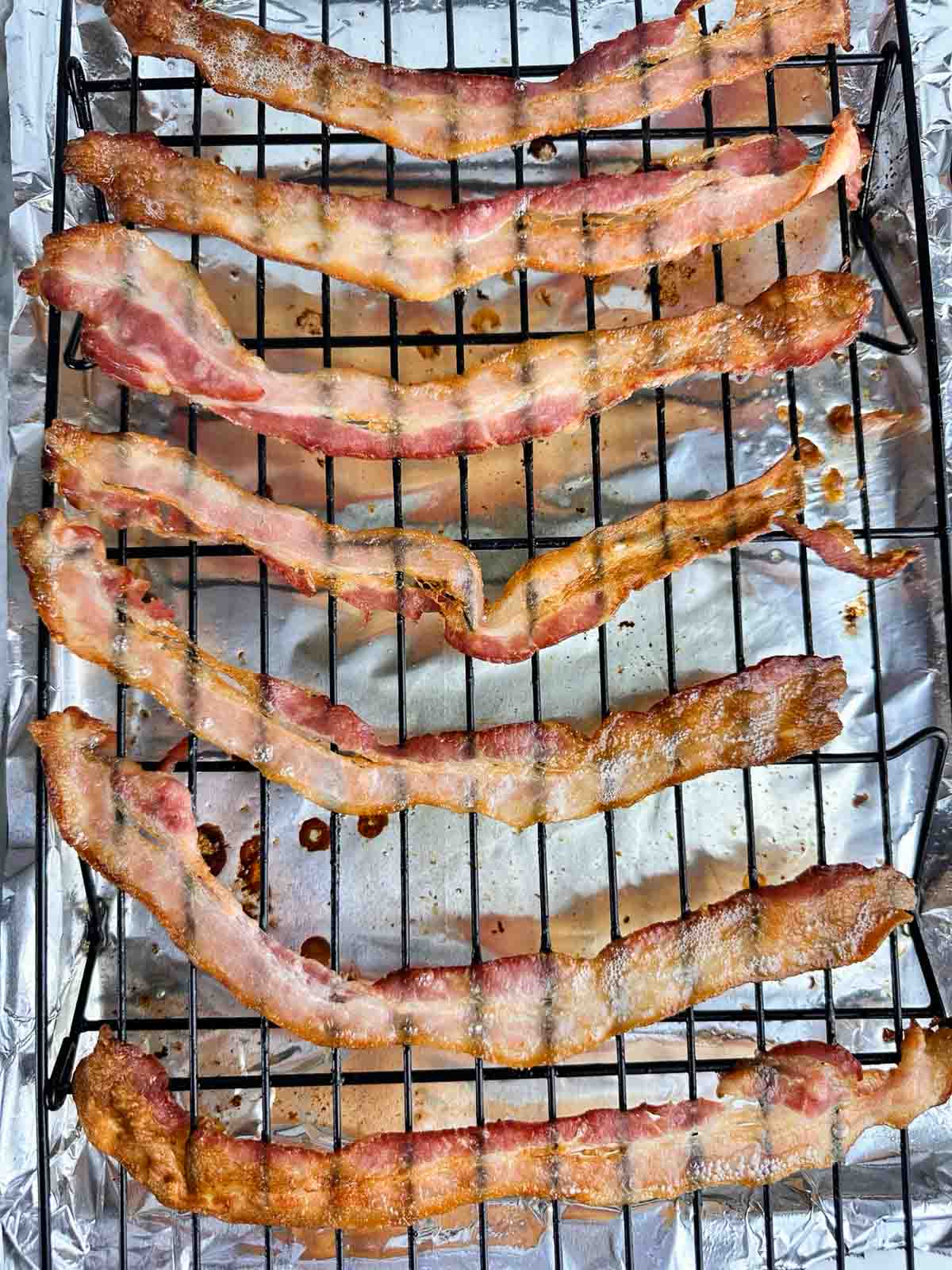 Crisp strips of bacon fresh out of the convection oven on a cooking rack set on top of a foil lined tray