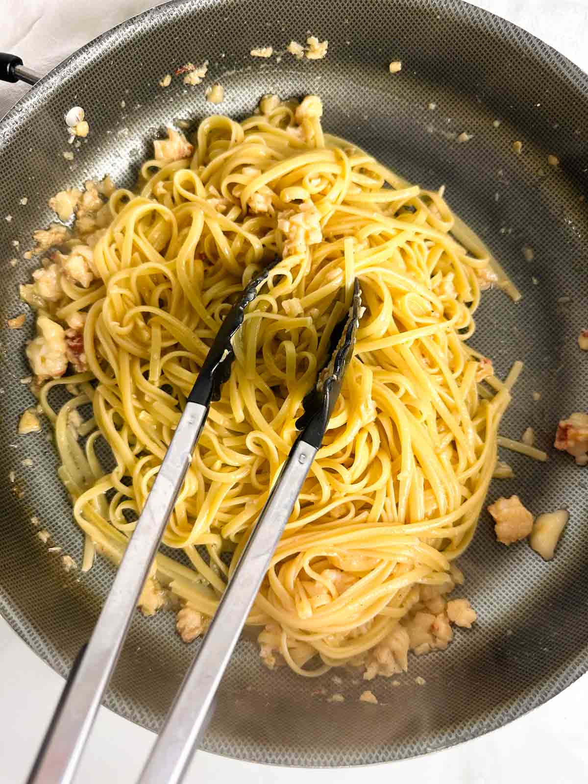Tossing cooked linguine noodles with lobster pieces in a sauce pan.