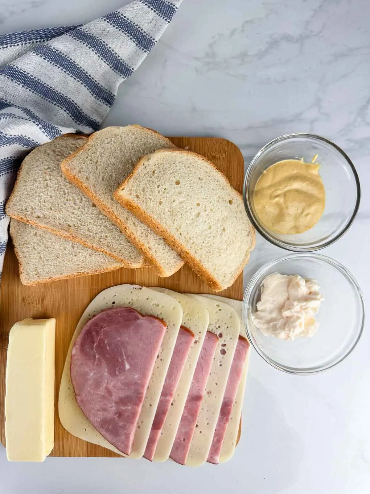 Ingredients for a ham and cheese panini: sturdy bread, condiments, butter, ham, and cheese