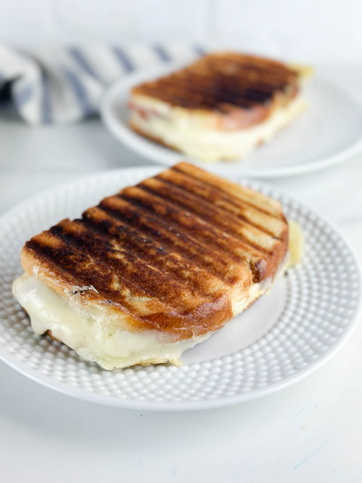 2 ham and cheese paninis on white plates