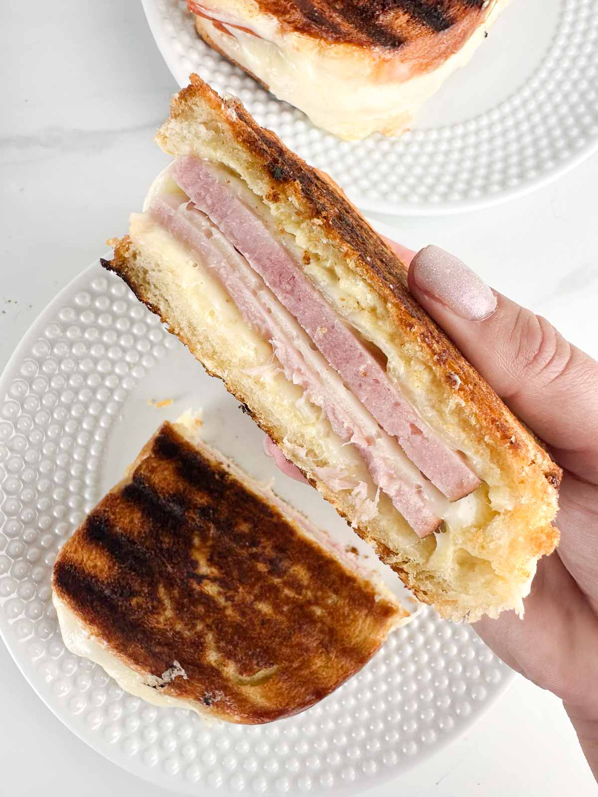A hand holding half a ham and cheese panini showing the layers of cheese and meat