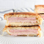 2 ham and cheese paninis cut in half and stacked showing the layers of cheese and meat on white plates
