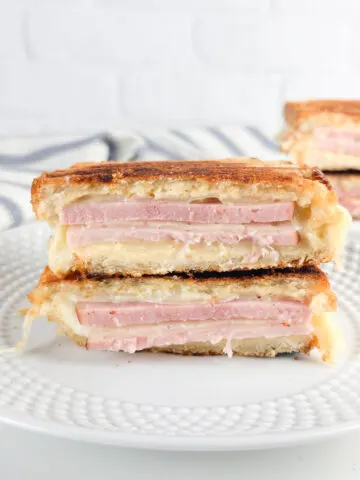2 ham and cheese paninis cut in half and stacked showing the layers of cheese and meat on white plates
