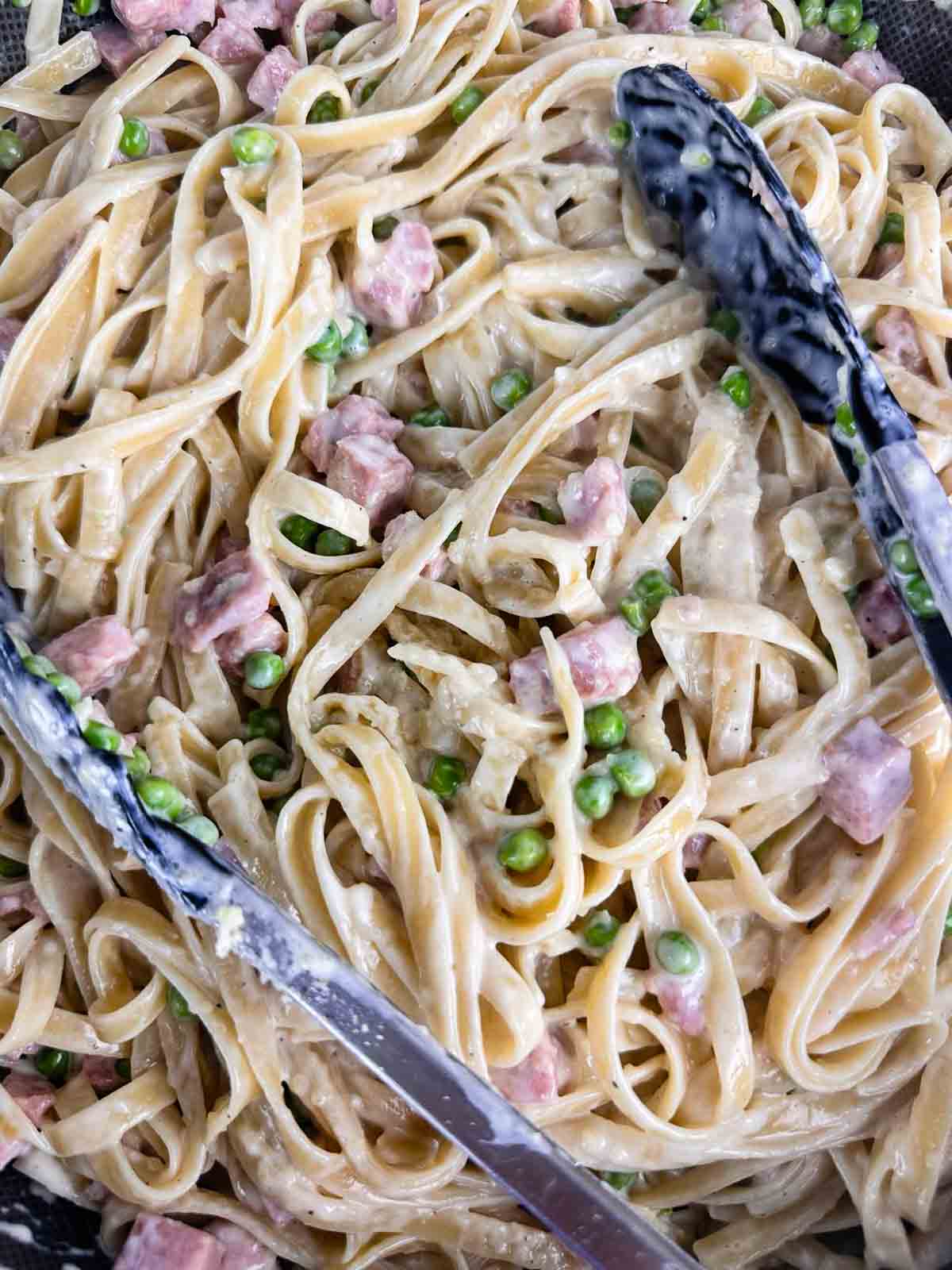 Add the heavy cream and Parmesan cheese to the pasta with ham and peas and toss it until the noodles are coated.