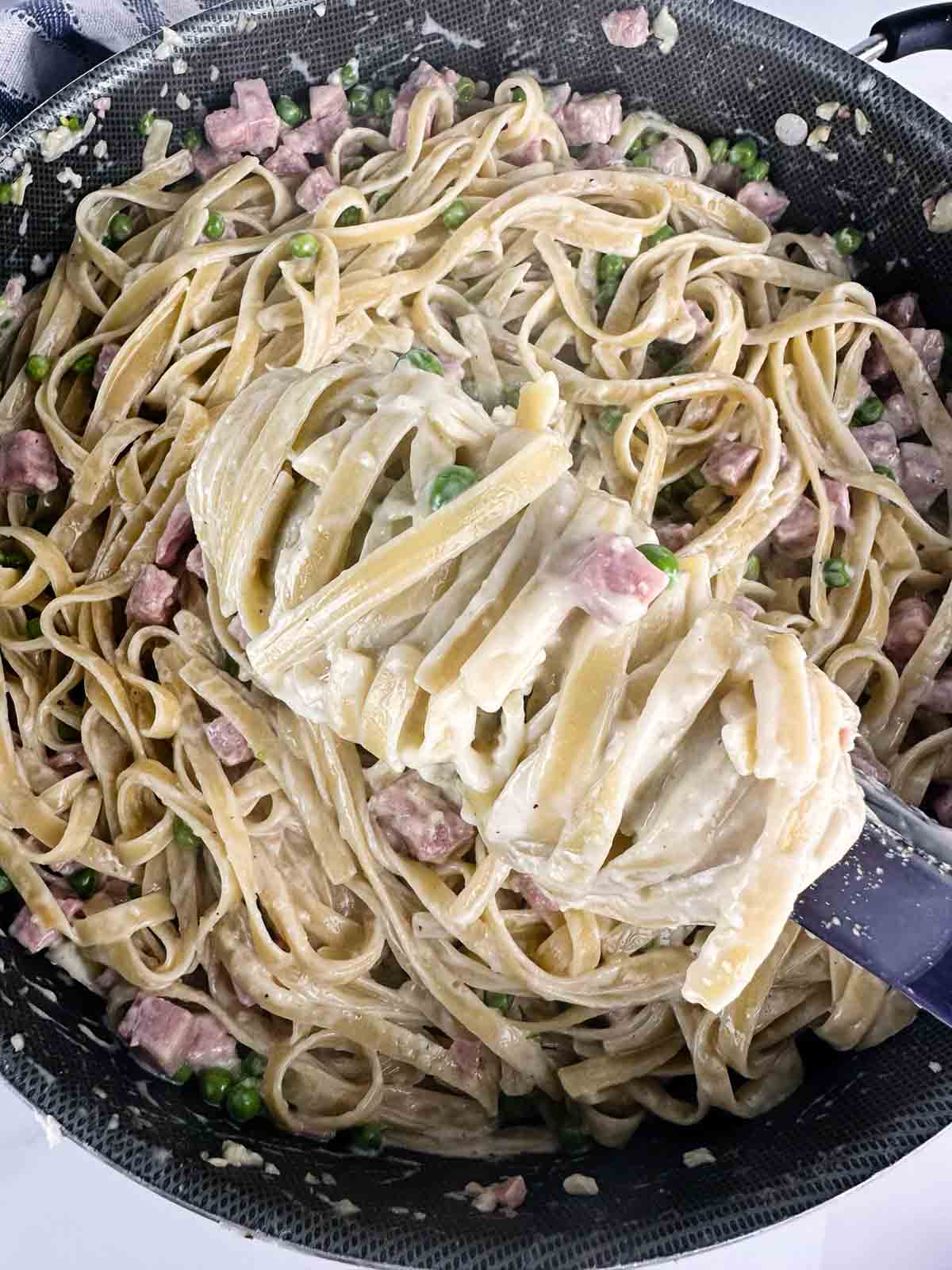 Pasta with ham and peas being twirled with tongs before serving