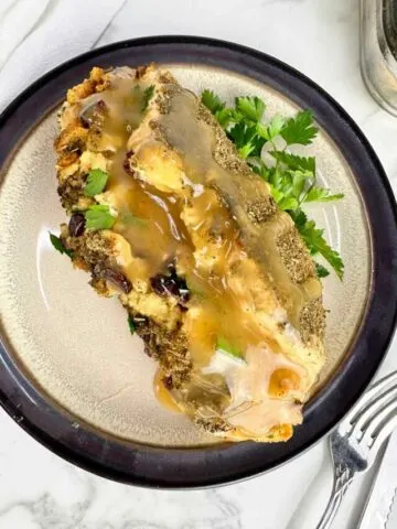 One plated stuffed chicken breast with stuffing and gravy served from a baking dish are ready to be served for dinner.